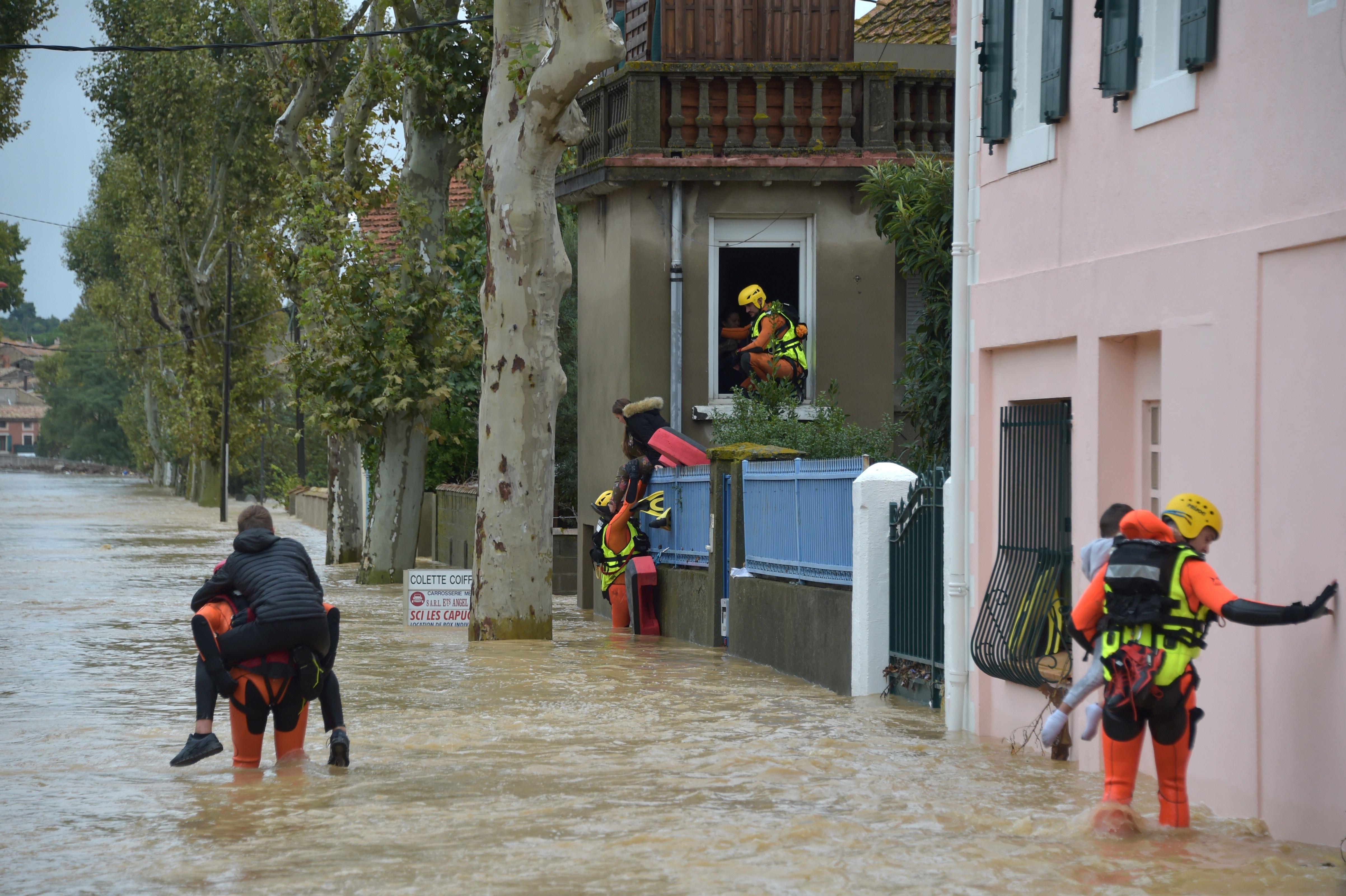 Des pompiers évacuent les habitants du village de Villegailhenc, dans l’Aude, inondé en octobre 2018. Équipés de combinaisons et de casques, ils portent les enfants dans les bras et sur leur dos. L’eau, qui leur arrive au genou, a un débit important.