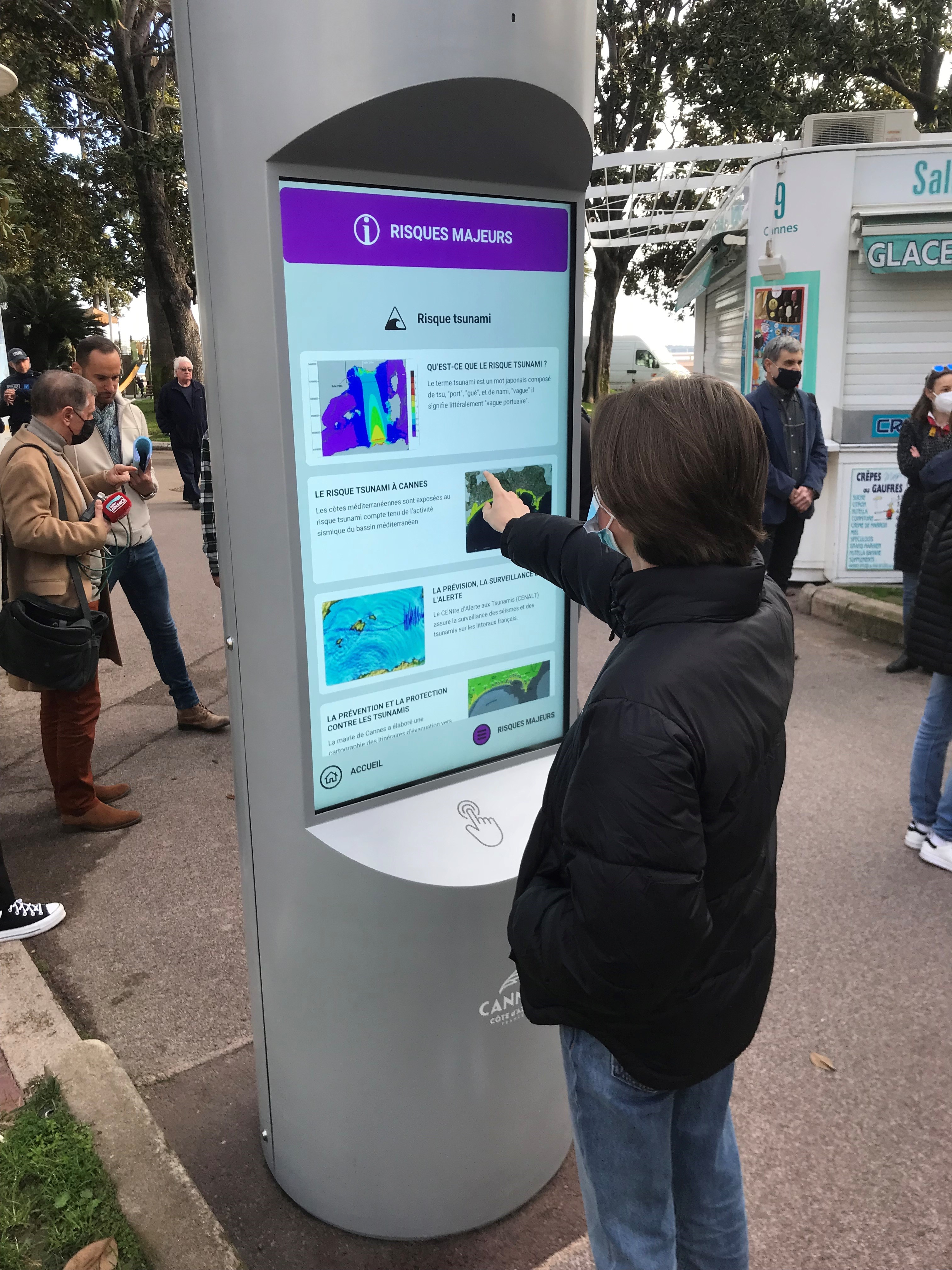 Photo montrant une personne qui utilise une borne numérique sur les risques majeurs, mise en place par la ville de Cannes, pour les habitants et les touristes.